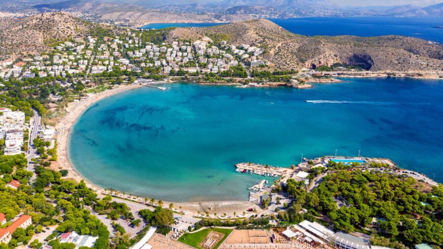 Aerial view of Mediterranean coastal bay with beach, marina, villas, and vibrant blue waters.