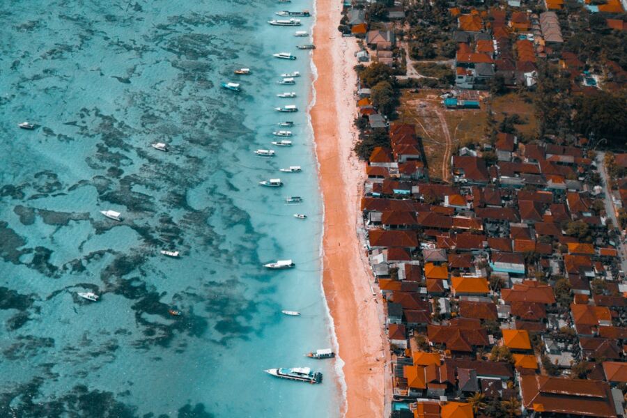 Aerial view of vibrant coastal Nusa Lembongan landscape with beach, boats, turquoise waters, and charming residences.