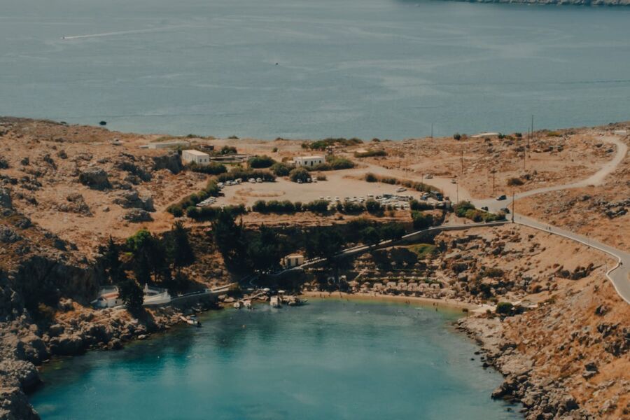 Scenic coastal landscape with rocky terrain, clear cove, boats, whitewashed buildings, and golden hills.