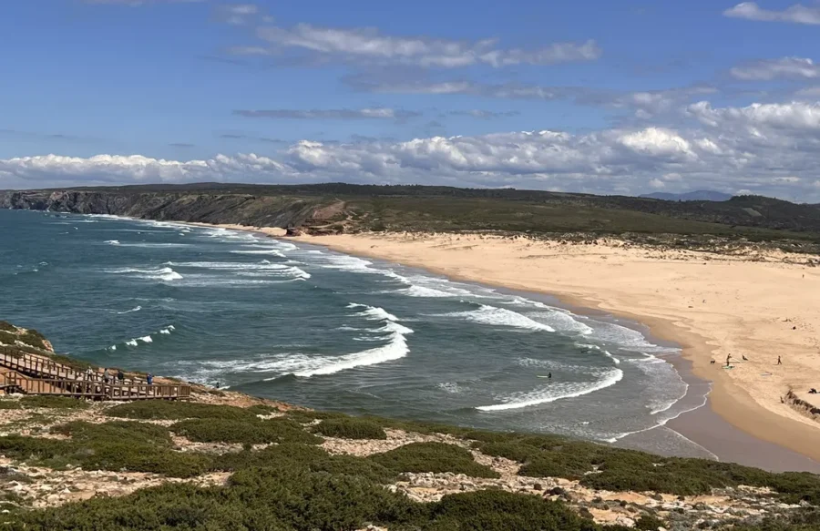 Carrapateira aerial beach view with winding coastal trail and surfers.