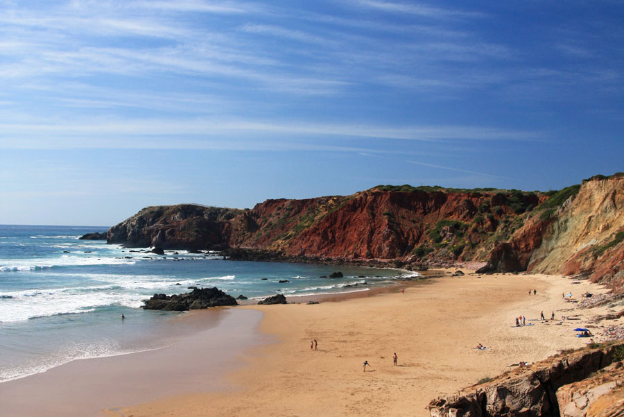 Praia do Amado beach with golden sand, rugged cliffs, and turquoise Atlantic waves, Algarve.