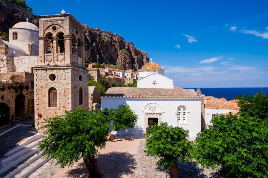 Mediterranean coastal church with bell tower, golden-tiled dome, whitewashed facade and sea view.