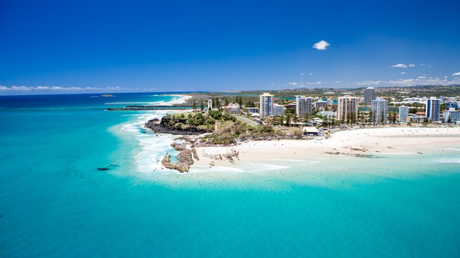 Aerial view of Coolangatta beach, turquoise ocean, coastal city skyline and sandy shoreline.