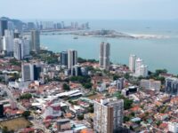 Aerial view of modern coastal city skyline with bay, high‑rise buildings and waterfront development.