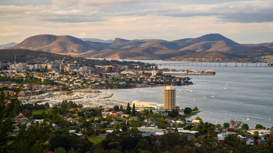 Hobart waterfront cityscape with harbor, bridge, marina, boats, suburbs and mountain backdrop at dusk.