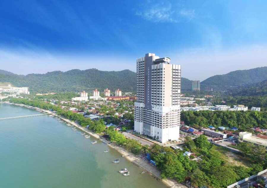 Coastal Penang high rise hotel overlooking beach, fishing boats, city skyline and lush green hills.