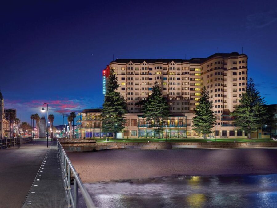 Luxury beachfront hotel on Adelaide coastal promenade at dusk with lights reflecting on calm water.