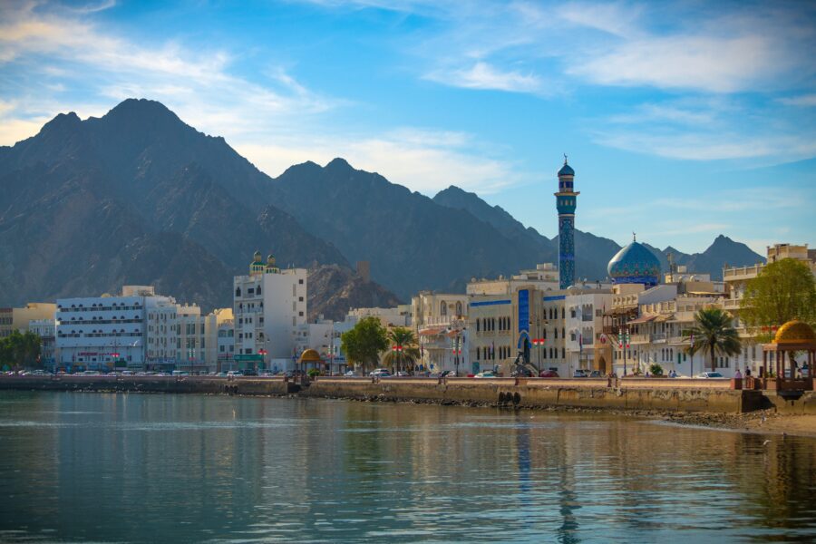 Muttrah waterfront cityscape with blue-domed mosque, calm turquoise water and rugged mountains in Oman.