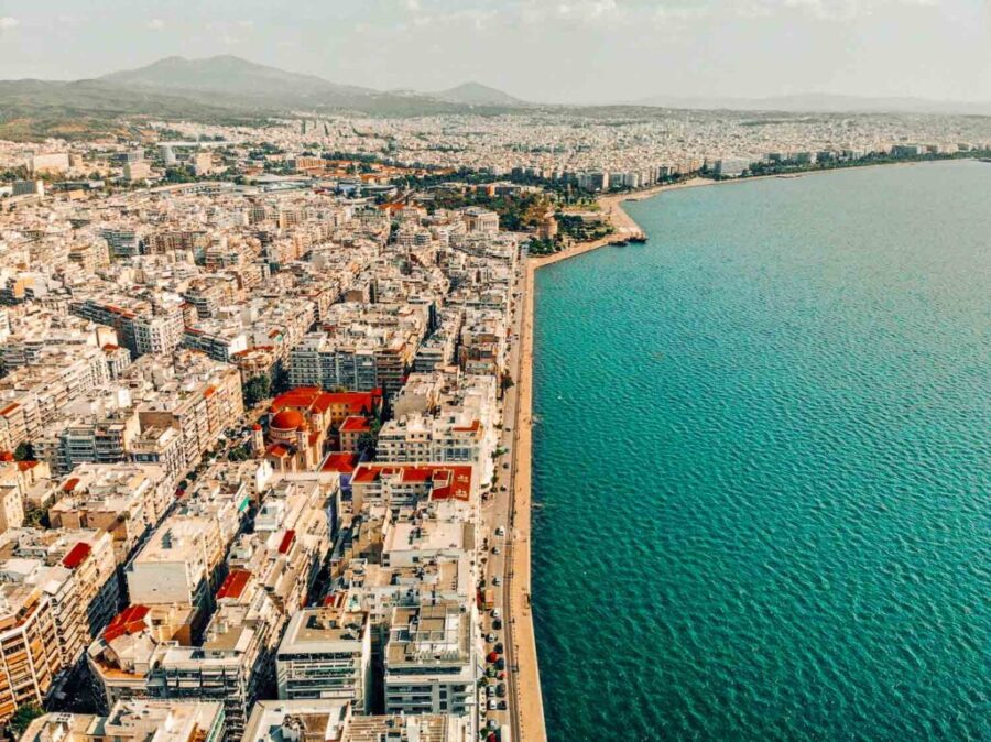 Aerial view of Thessaloniki: blending urban architecture, turquoise sea, Mediterranean style, lush hills.