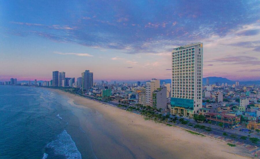 Aerial sunrise view of Da Nang beach skyline with oceanfront hotels, mountains and pastel sky.