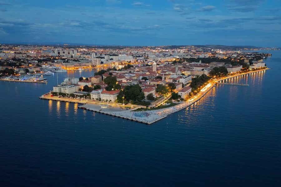 Aerial view of vibrant coastal city at dusk with illuminated buildings and calm sea.