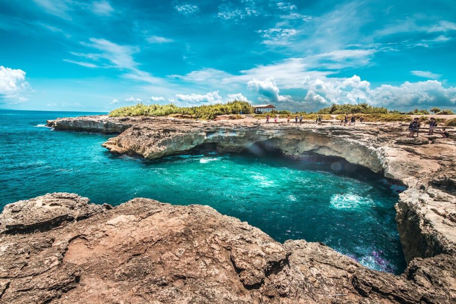 Turquoise ocean cove with waves crashing against rocky cliffs on Nusa Ceningan coastline.