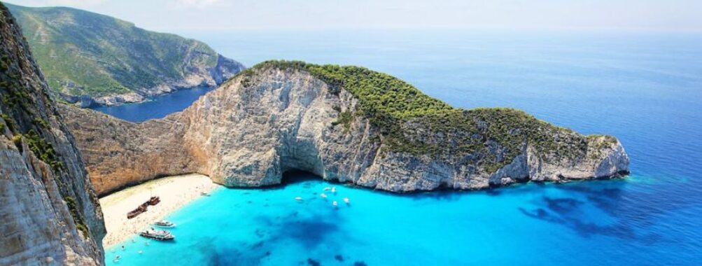 Dramatic coastal cliffs with azure waters, secluded beach, boats, and vibrant landscape.