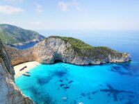 Dramatic coastal cliffs with azure waters, secluded beach, boats, and vibrant landscape.