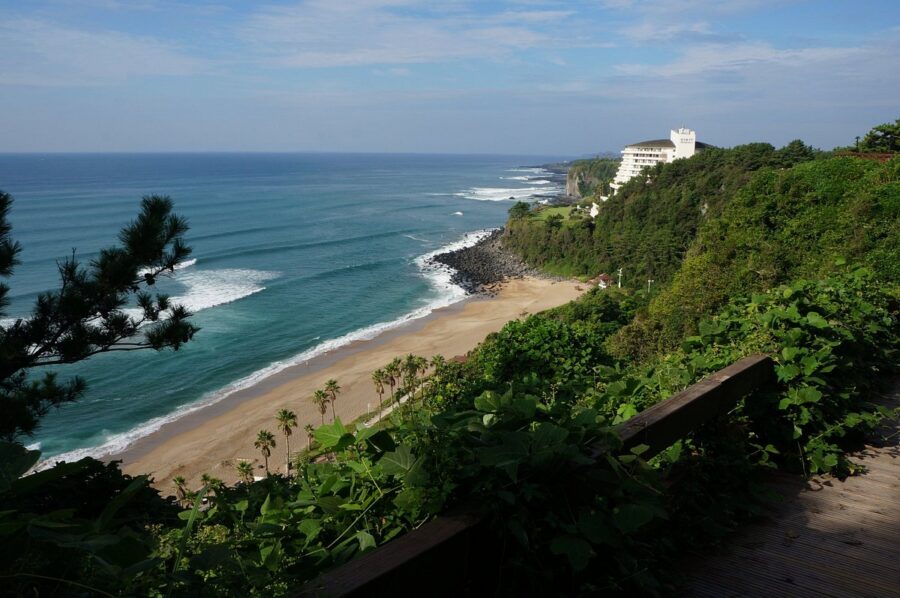 Scenic Jungmun Beach coastal cliffs, turquoise ocean waves, tropical palm trees and luxury seaside resort.