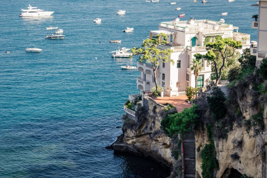 Elegant white villa on a Mediterranean Posillipo cliff with boats and lush greenery.