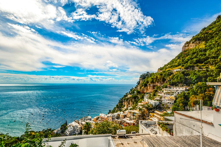 Aerial view of Mediterranean cliffside village with terraced houses and turquoise sea.