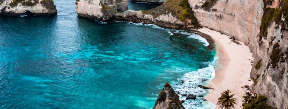 Breathtaking Bali coastal landscape with cliffs, turquoise waters, sandy beach, and lush greenery.