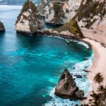 Breathtaking Bali coastal landscape with cliffs, turquoise waters, sandy beach, and lush greenery.
