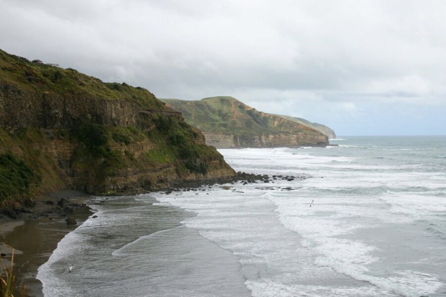 Majestic coastal cliffs above the ocean with beach and seagulls in tranquil scenery.