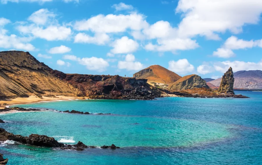 Breathtaking Galápagos coastal landscape with turquoise waters, rugged cliffs, and mountainous backdrop.
