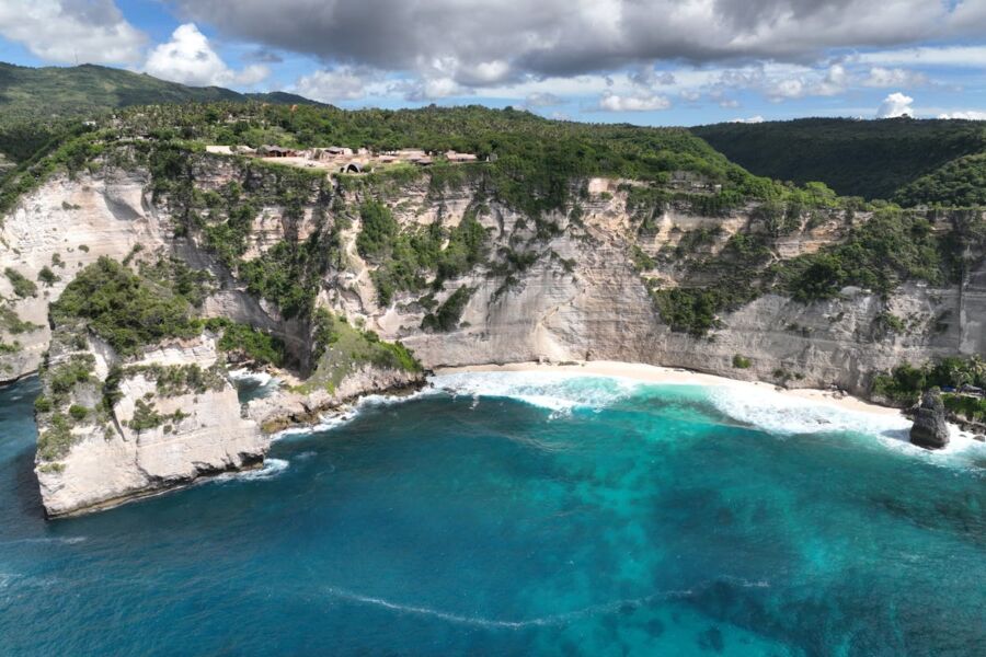 Dramatic Nusa Penida coastal cliffs with lush greenery, turquoise waters, and structures overlooking the ocean.