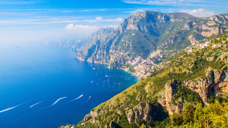 Dramatic coastal cliffs and turquoise bay with hillside village on the Amalfi Coast.
