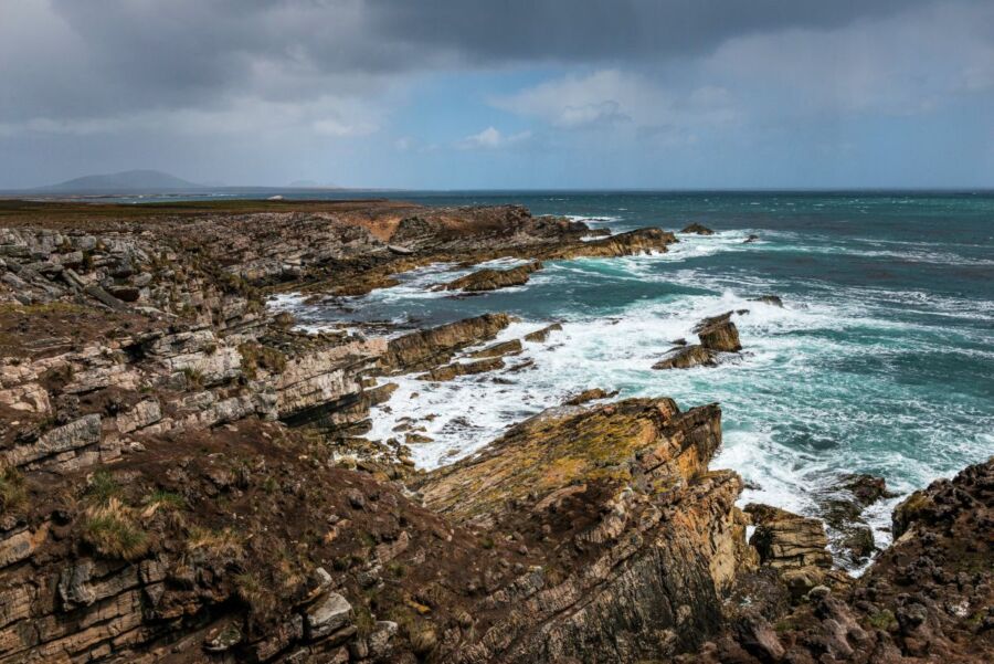 Dramatic rocky coastline with waves, cliffs, and overcast sky in a dynamic seascape.