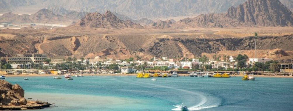 Turquoise Red Sea bay with speedboat, resort town shoreline and desert mountains in Egypt.