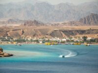 Turquoise Red Sea bay with speedboat, resort town shoreline and desert mountains in Egypt.