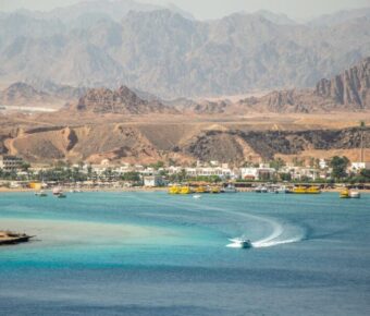 Turquoise Red Sea bay with speedboat, resort town shoreline and desert mountains in Egypt.