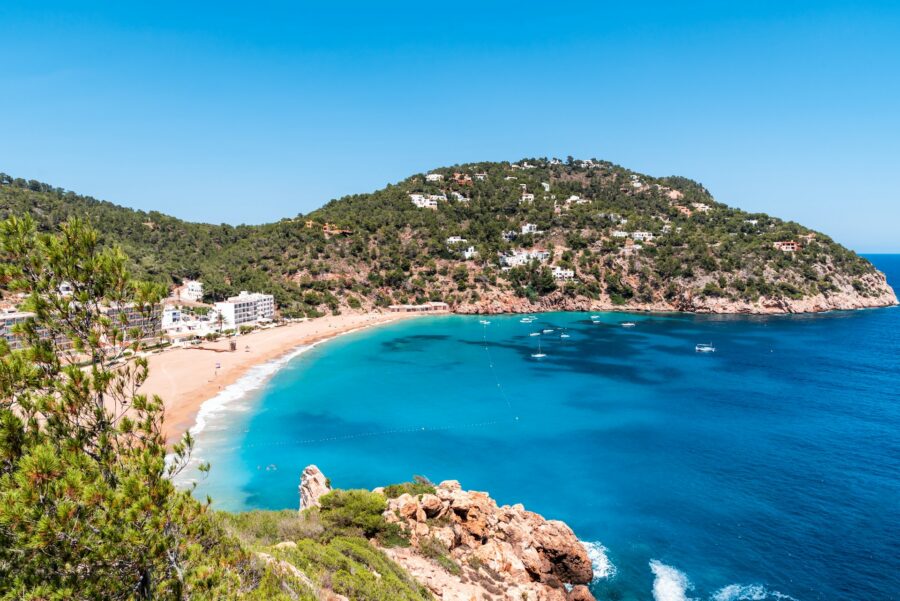Idyllic Mediterranean beach with turquoise waters, lush hillside, and quaint coastal buildings.