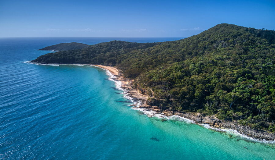 Aerial view of Noosa National Park coastal headland with turquoise ocean, secluded beach, and lush forest.