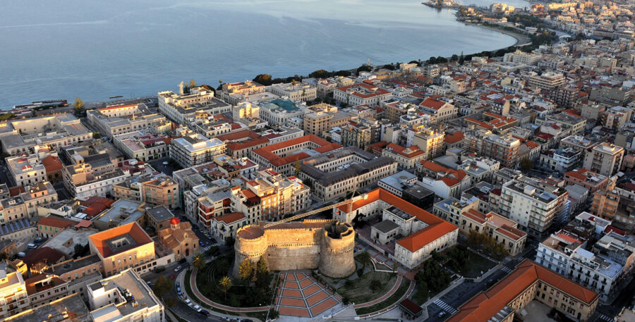 Reggio Calabria aerial view of coastal fortress, terracotta rooftops, and Mediterranean sea.