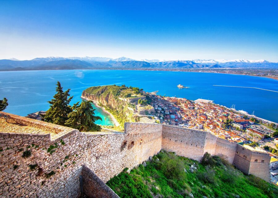 Nafplio coastal fortress overlooking bay, red-tiled town, turquoise cove and snow-capped mountains.