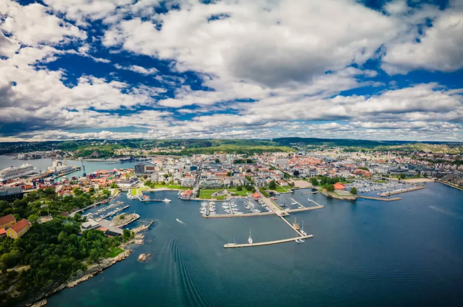 Aerial view of Kristiansand harbor with marinas, boats, waterfront city, and surrounding hills.