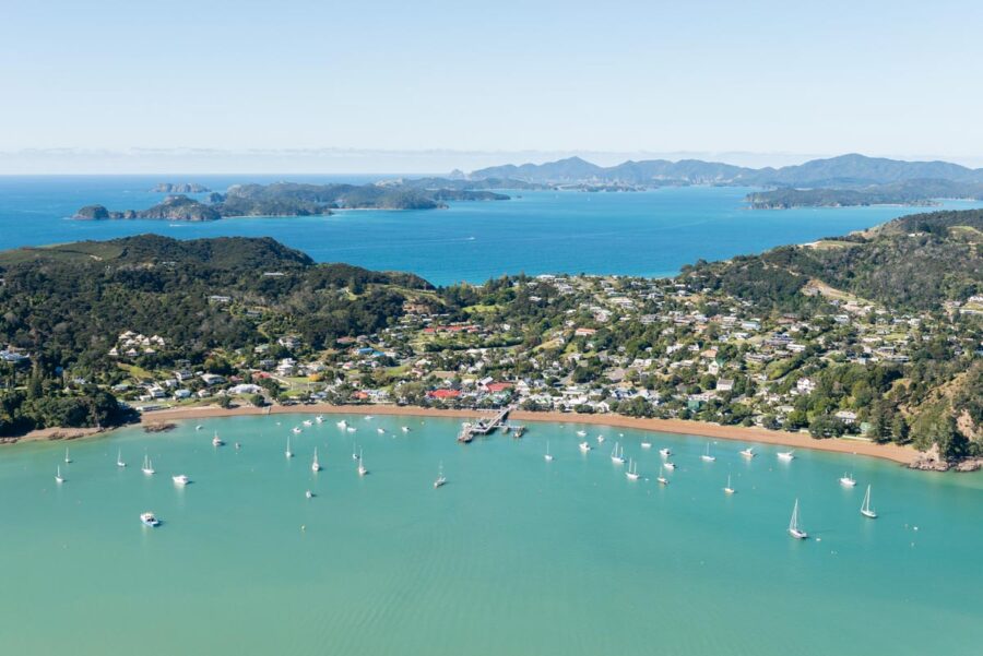 Aerial view of Russell coastal town, turquoise bay, sailboats, green hills and islands in New Zealand.