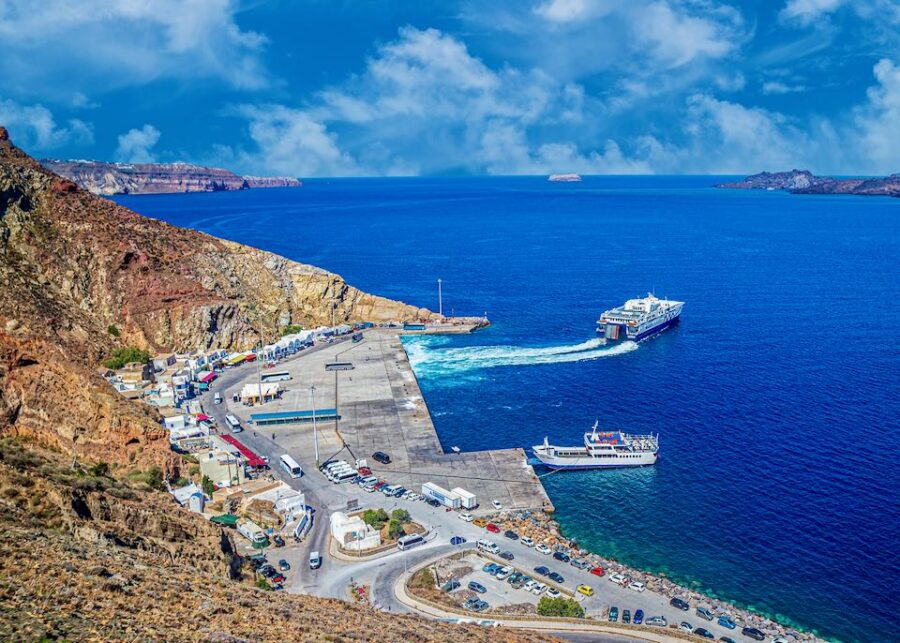 Coastal harbor scene with ferries, cliffs, and blue sea at Santorini Ferry Port, Greece.