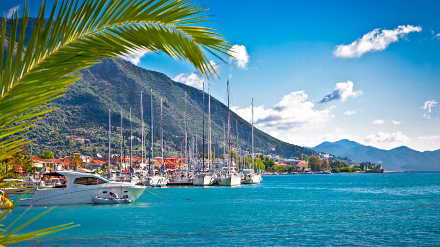 Tranquil marina scene with sailboats, lush mountains, and palm trees on a sunny day.
