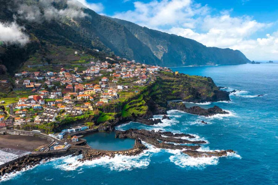 Madeira coastal village on terraced cliffs overlooking Atlantic Ocean with rocky shoreline and breakwater.