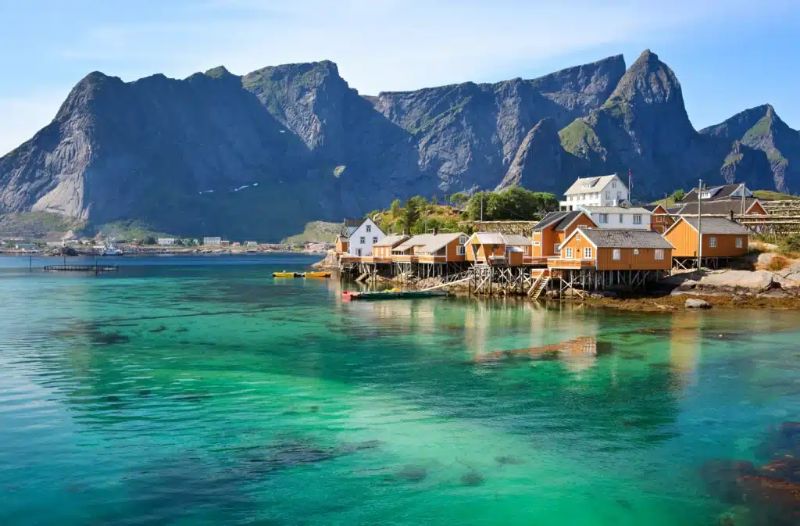 Scenic fishing village by mountains, turquoise waters, traditional rorbuer, and boats.