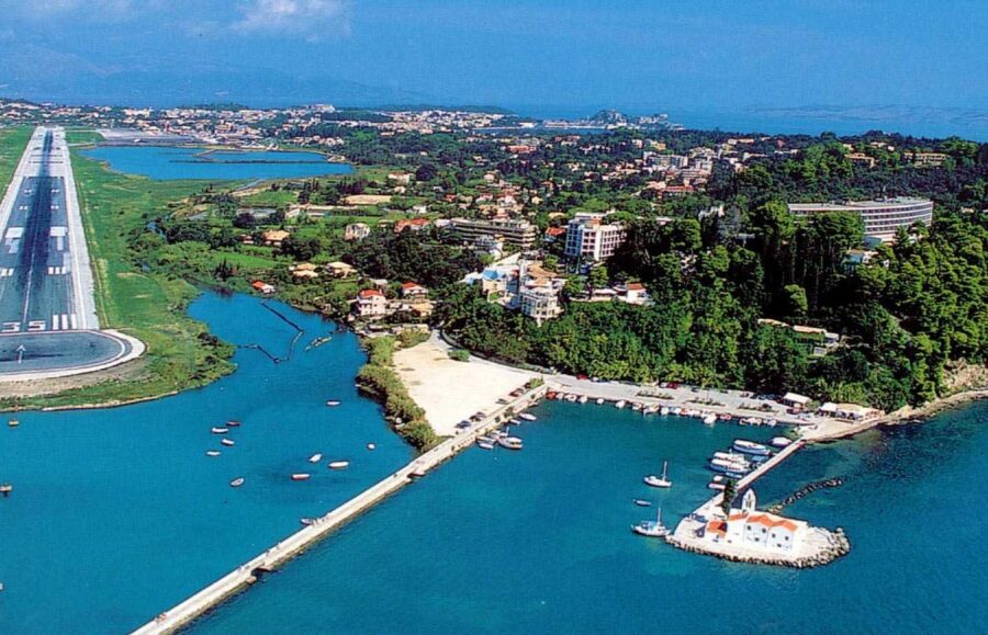 Aerial view of Acharavis coastal harmony: harbor, runway, residences, nature, sea, sky.