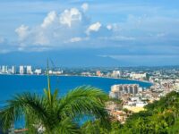 Panoramic view of coastal city skyline, vibrant ocean, lush greenery, and diverse architecture.
