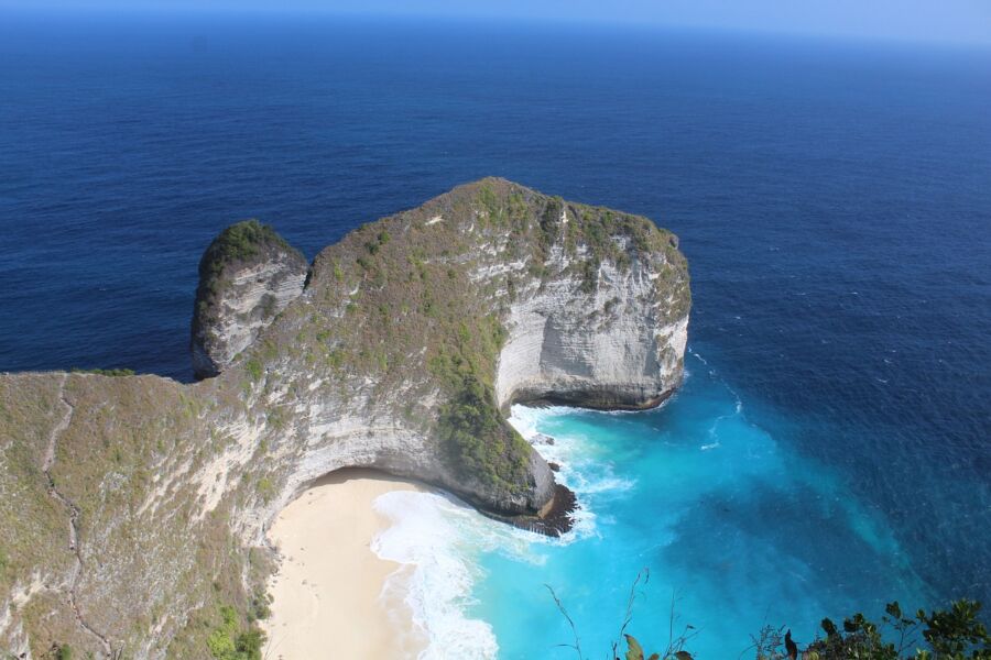 Nusa Penida stunning coastal rock formation in vibrant blue sea with lush greenery and sandy beach.