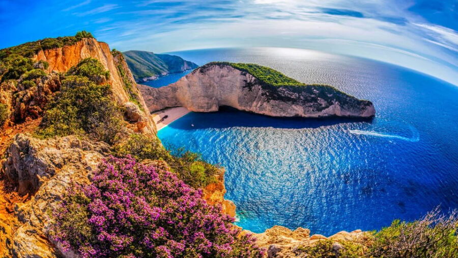 Majestic coastal cliffs, azure waters, vibrant flowers; a serene, breathtaking panoramic landscape.