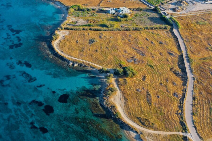 Aerial view of serene coastal landscape with blue sea, rocky shore, and isolated white house.