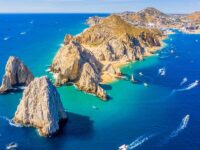 Aerial view of tropical coastline with azure ocean, rugged cliffs, and vibrant maritime activity.