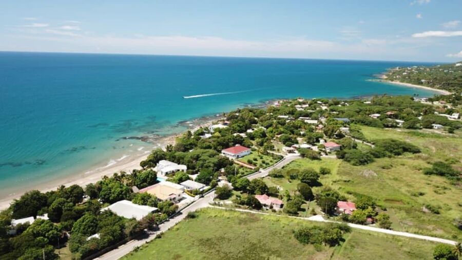 Picturesque coastal landscape with sandy beach, rocky outcrops, turquoise sea, and charming residential area.