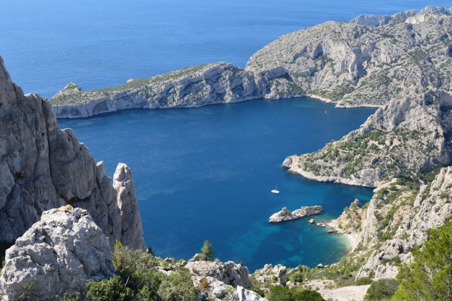 Stunning coastal landscape with cliffs, azure cove, sailboat, and vibrant vegetation.