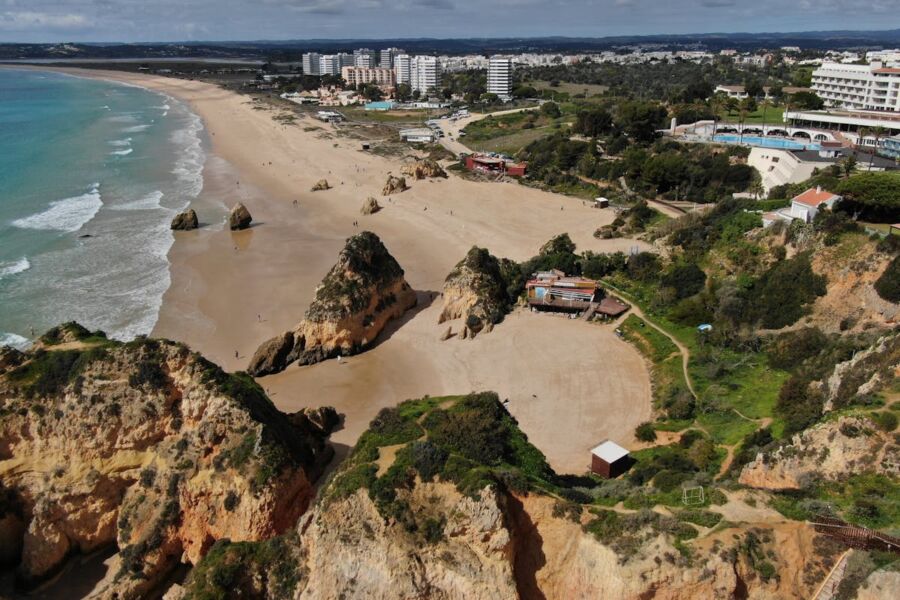 Stunning Alvor coastal landscape with sandy beach, rugged cliffs, sparkling ocean waters, and modern buildings.